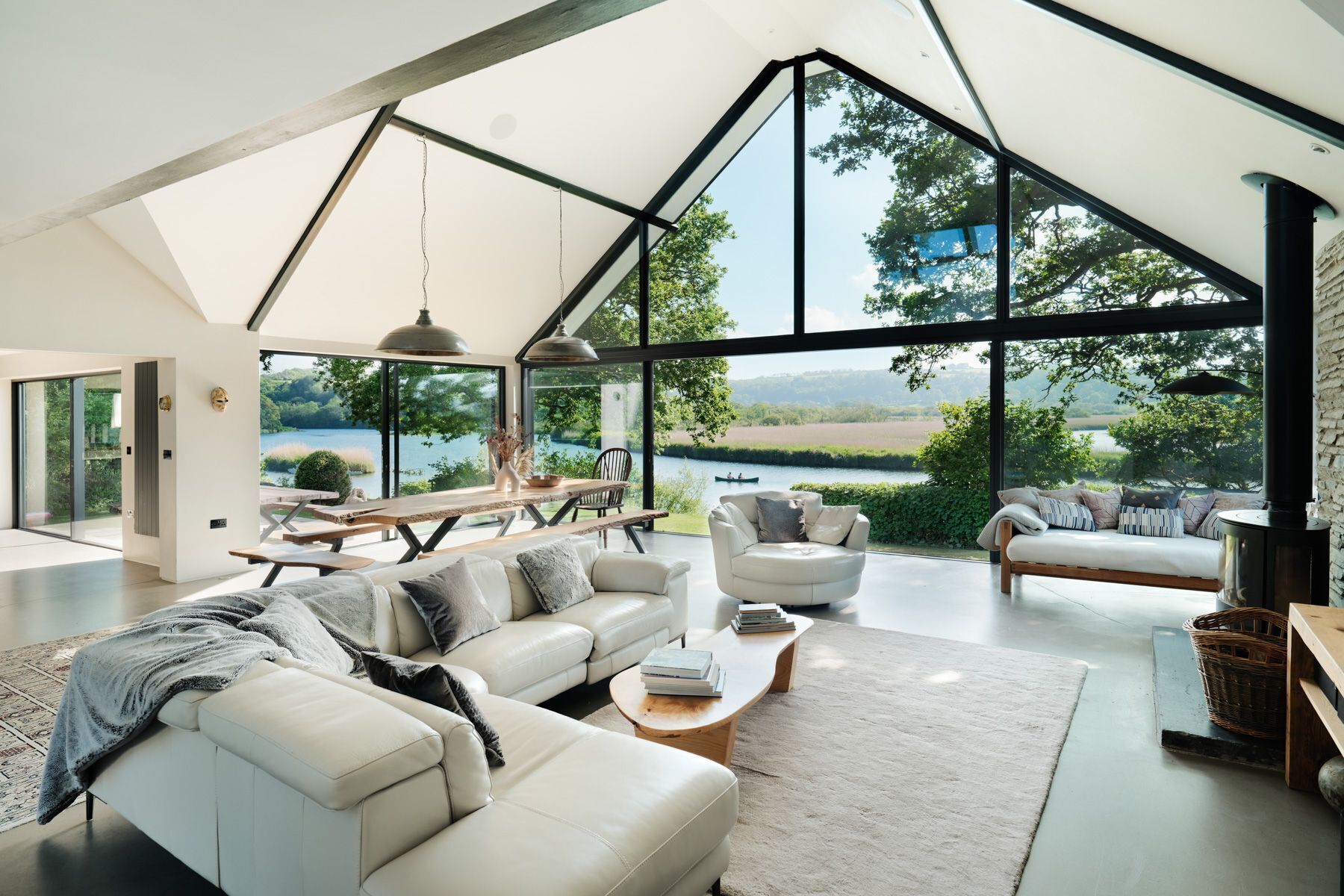 A spacious living area with a large window overlooking a lake, a dining area with a table and chairs, and a seating area with a sofa and armchairs.