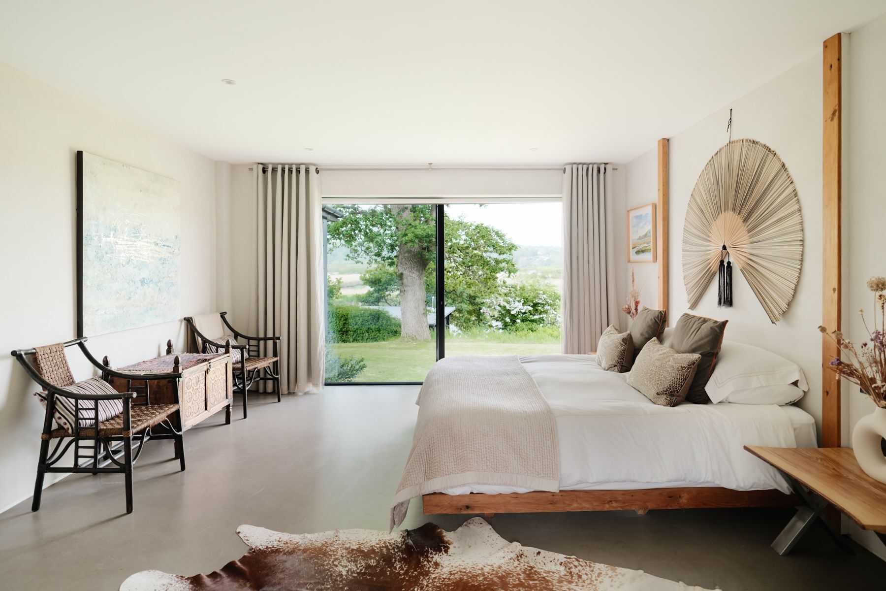 A bedroom with a large bed, a desk, and a view of the outdoors.