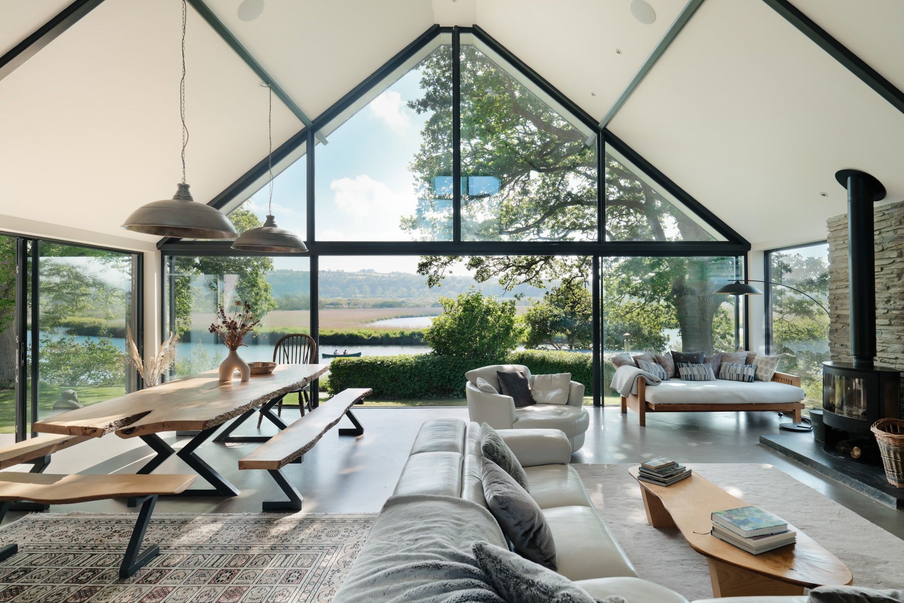 A spacious interior with a high ceiling, large windows, a dining area, seating, and a fireplace.