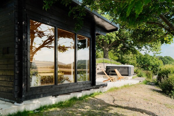 A modern cabin with large windows, a grill, and outdoor seating.