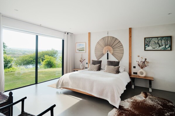Un dormitorio moderno con una cama grande, vistas al exterior, un ventilador de pared y un cuadro.