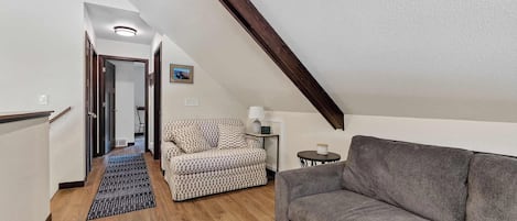 Ein Loftsessel mit hohen Decken, einer Holztreppe, einem gemusterten Sofa, einem grauen Sofa und einem kleinen Tisch mit einer Lampe.