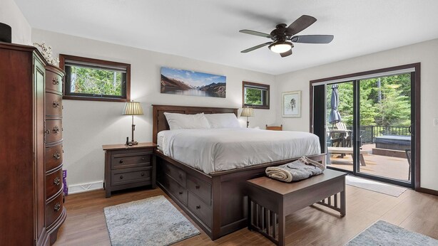 Une chambre à coucher comprenant un lit, une table de chevet, une commode, un ventilateur de plafond et une vue sur l’extérieur grâce à une porte-fenêtre coulissante.