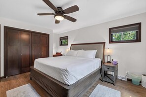 Une chambre à coucher avec un grand lit, un ventilateur de plafond, une table de chevet avec une lampe et une fenêtre avec des stores.