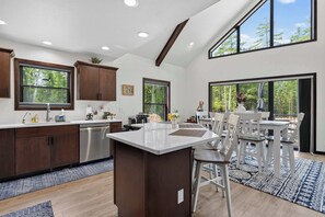 Une cuisine moderne dotée d’un îlot central, de meubles en bois et de grandes fenêtres offrant une vue sur l’extérieur.