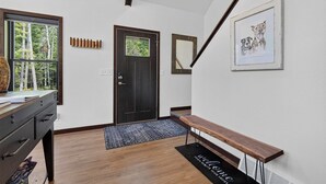 Un couloir avec un banc en bois, une porte dotée d’une fenêtre, un tableau encadré accroché au mur et un bureau sur lequel se trouve un vase.