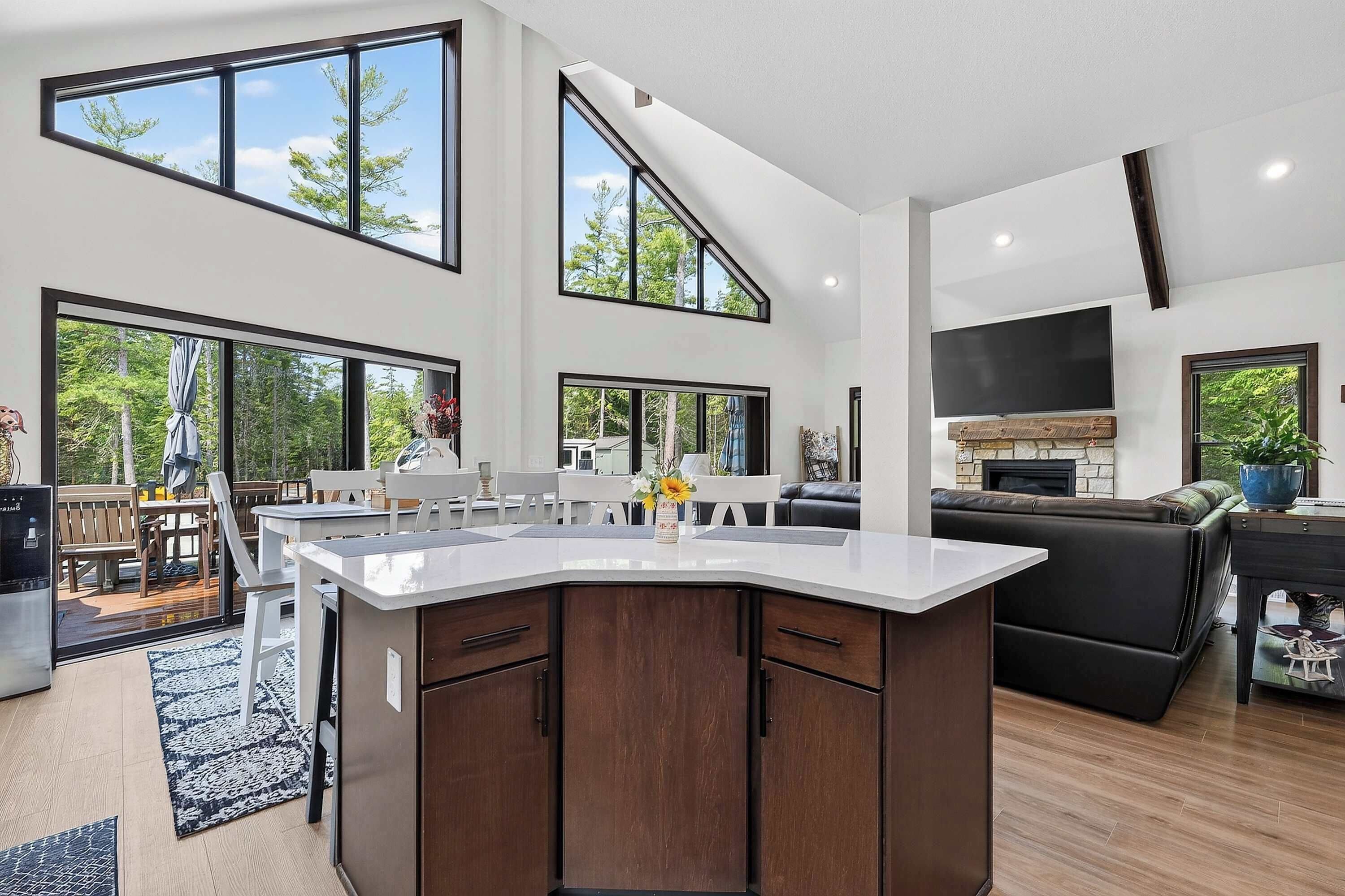 A spacious living area with a large kitchen island, a fireplace, and multiple windows offering views of the outdoors.