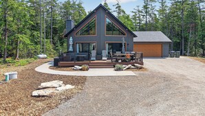 Une maison moderne à deux étages, dotée d’une grande terrasse, d’un garage et surplombant un paysage boisé.