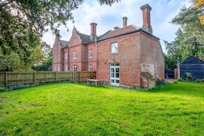 A brick house with a large backyard, a wooden fence, and a shed.