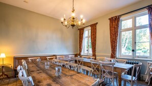 Une salle à manger avec une grande table en bois, des chaises blanches, un lustre et une vue par la fenêtre.