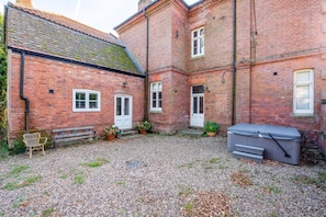 A brick building with a gravel courtyard, a bench, potted plants, and a hot tub.