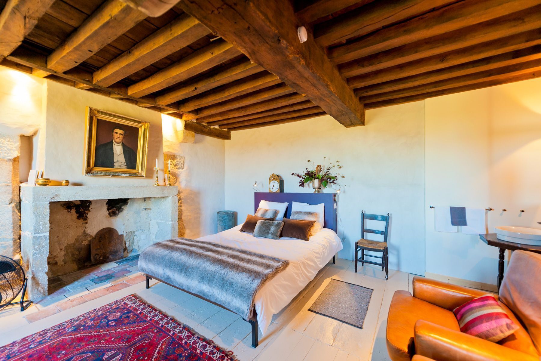 Un dormitorio con cama, una silla, un sofá, una chimenea y un reloj en la pared.