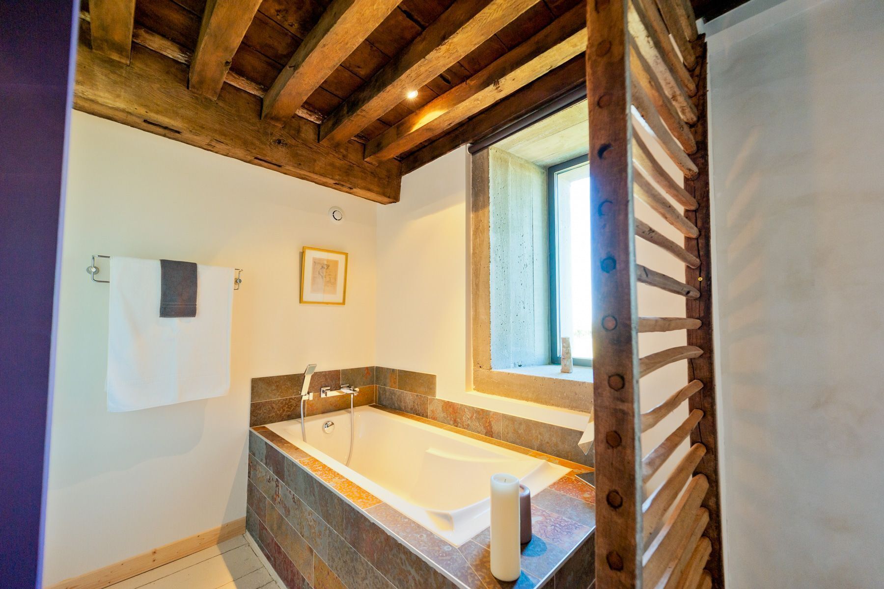 A bathroom with a bathtub, a window, and wooden beams on the ceiling.