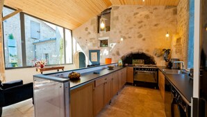 A modern kitchen with a stone wall, wooden ceiling, and a built-in oven. - Mounicat - Four Bedroom Villa, Sleeps 10 (Baleyssagues)