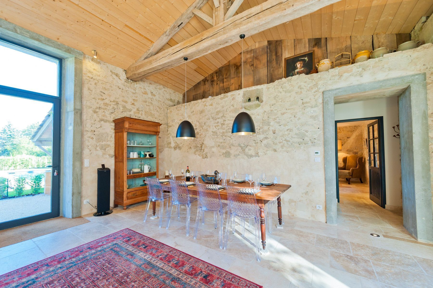 Un coin repas avec une table en bois, des chaises transparentes, un tapis à motifs et un mur en pierre.