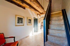 Un couloir avec un escalier en bois, une chaise rouge et des tableaux encadrés accrochés au mur.