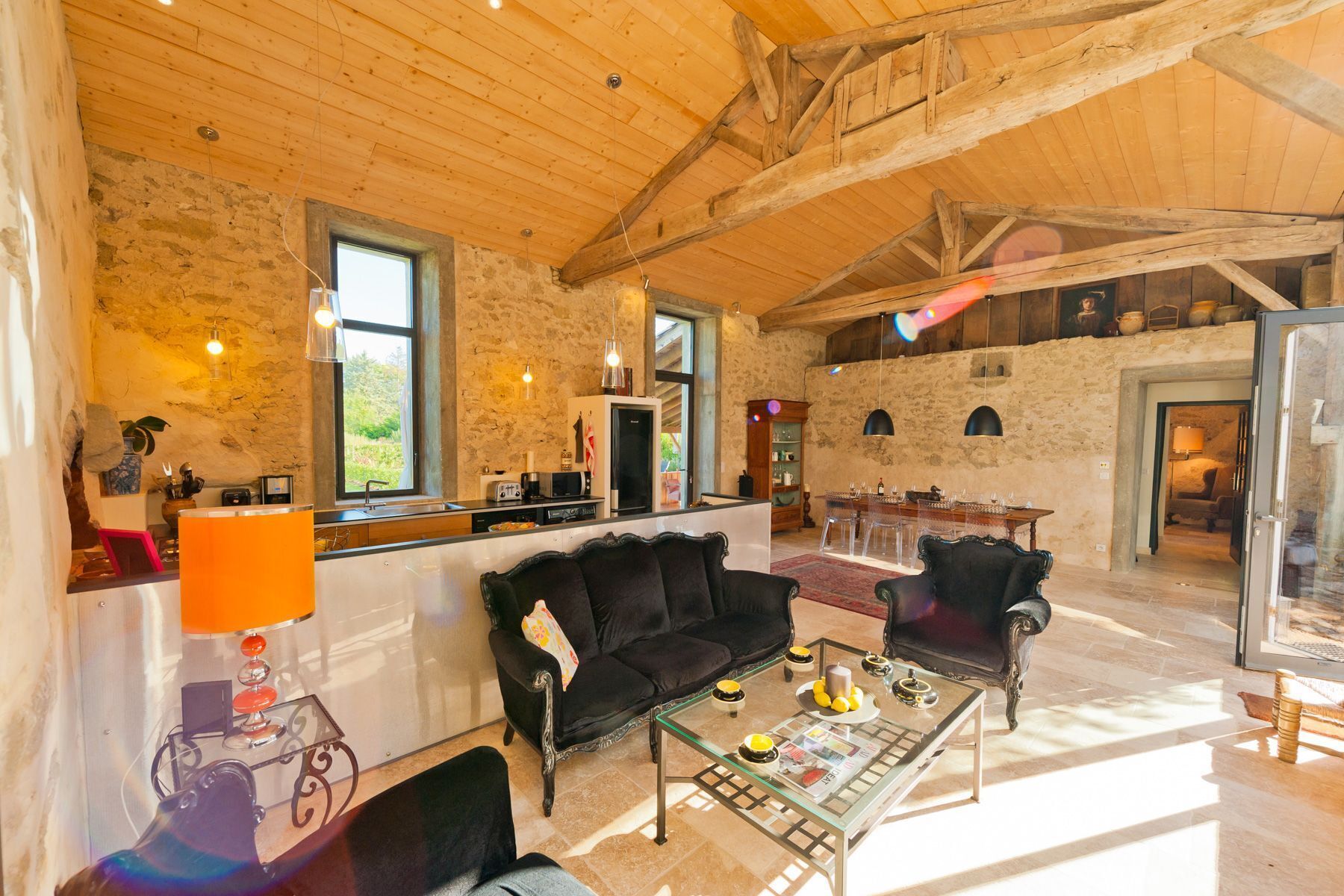 Un vaste espace de vie doté d’un haut plafond, de murs en pierre et d’un coin repas avec des tables en verre transparent.