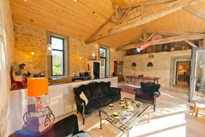 Un vaste espace de vie doté d’un haut plafond, de murs en pierre et d’un coin repas avec des tables en verre transparent.
