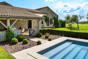 Uma casa de pedra com piscina, área de estar ao ar livre e um jardim bem cuidado.