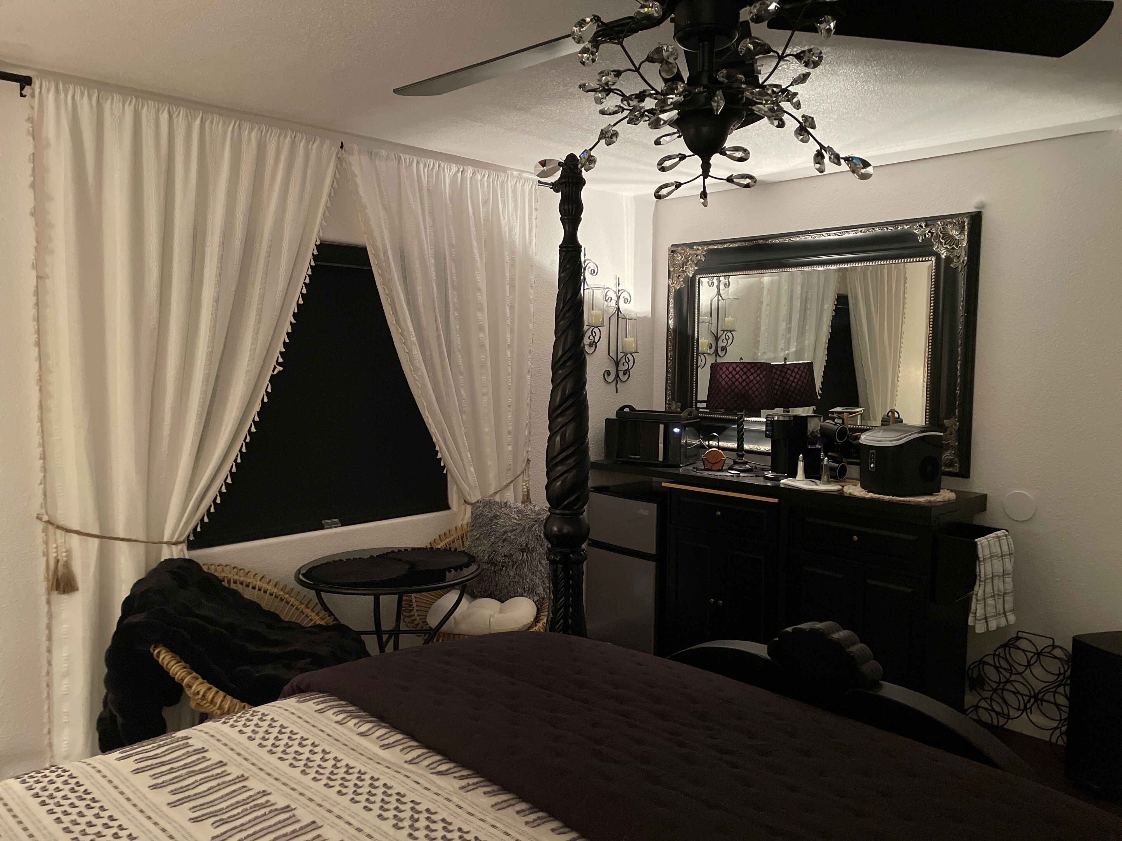 A bedroom with a bed, a dresser, a mirror, a ceiling fan, and a window with curtains.