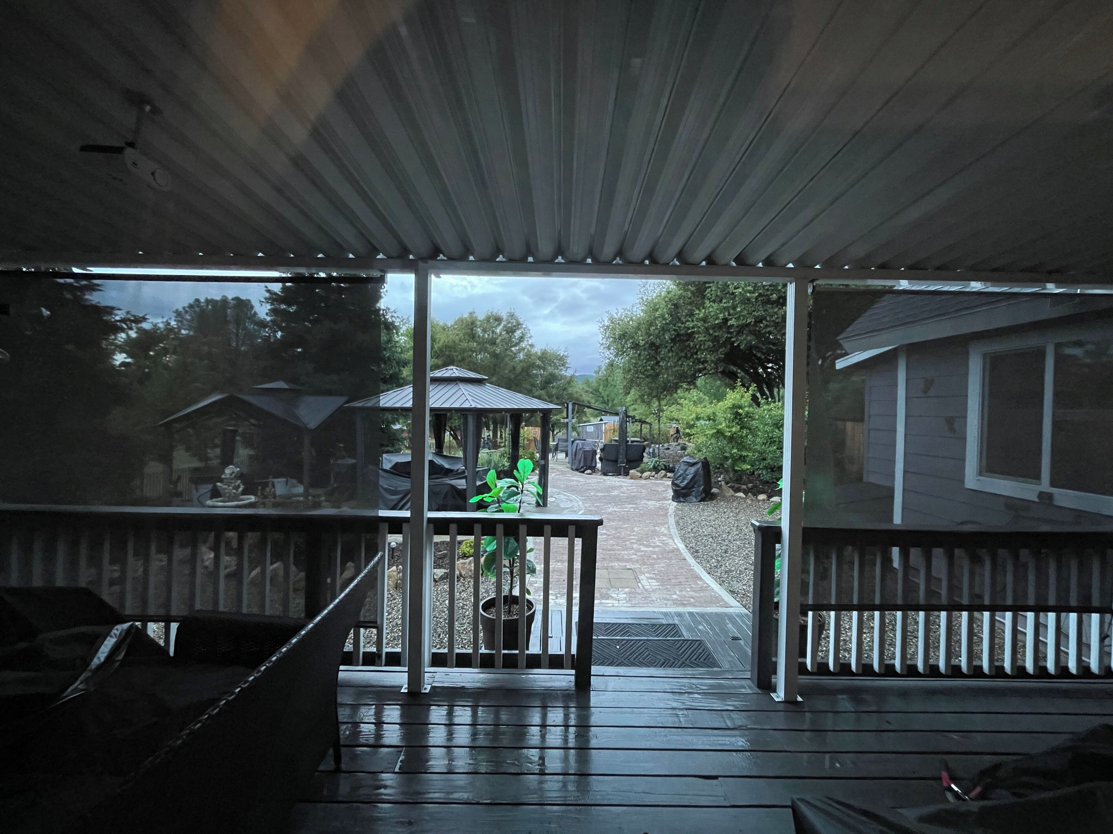 A covered outdoor area with a wooden deck, a gazebo, and a view of a backyard with a covered patio and a house.