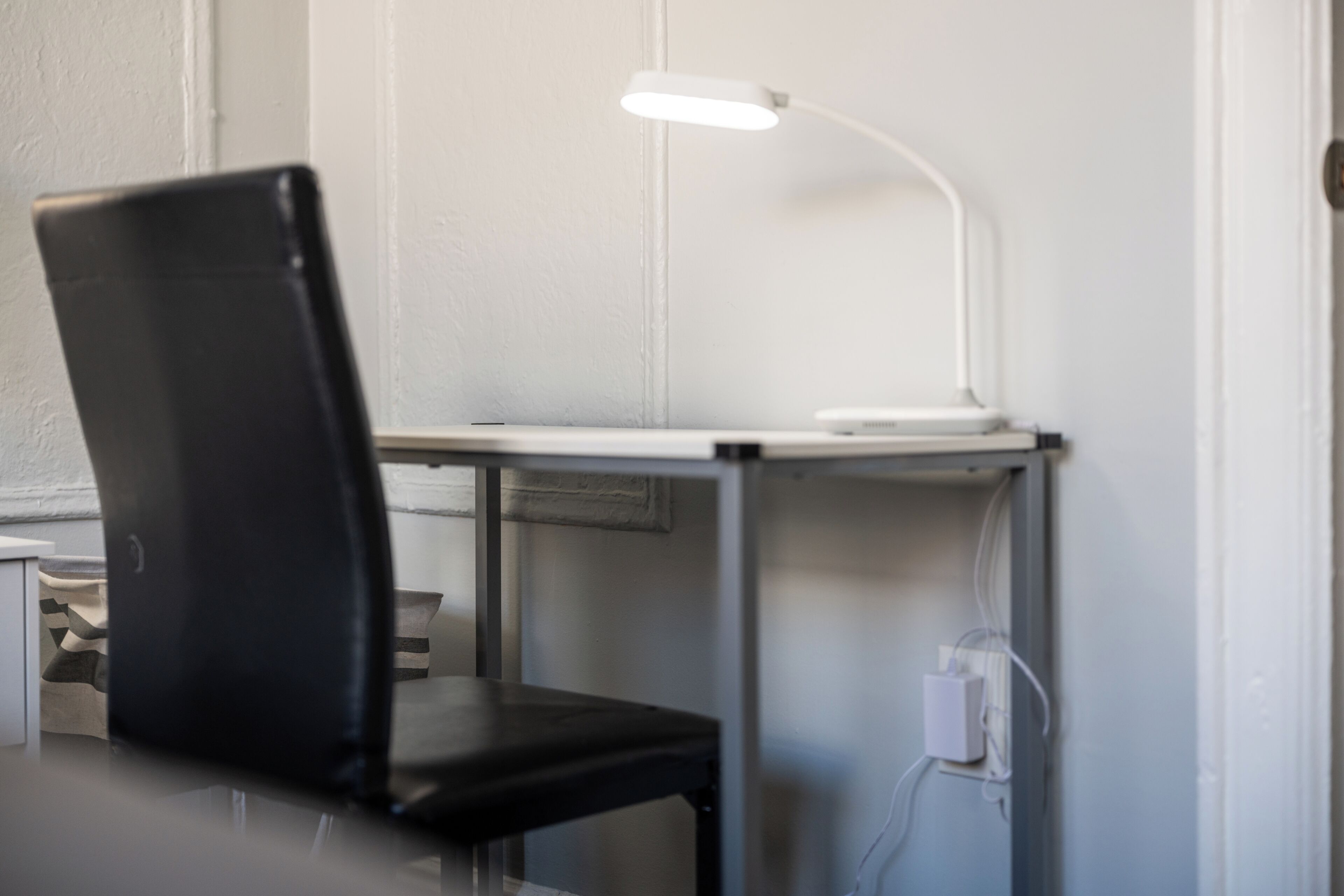 Ein Stuhl und ein Schreibtisch mit Schreibtischlampe, Steckdose und Wand-Schalter.