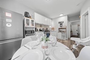 A modern kitchen with white cabinets, stainless steel appliances, and a dining area set for a meal. - Two Bedrooms • Coffee Station • Family Friendly (Jersey City)