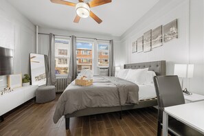 A modern hotel room with a large bed, a desk, and a ceiling fan. - Two Bedrooms • Coffee Station • Family Friendly (Jersey City)