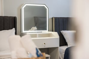 Ein Hotelzimmer mit Nachttisch, Spiegel mit LED-Beleuchtung, weißer Schublade und Bett mit weißer und dunkelgrauer Bettwäsche.