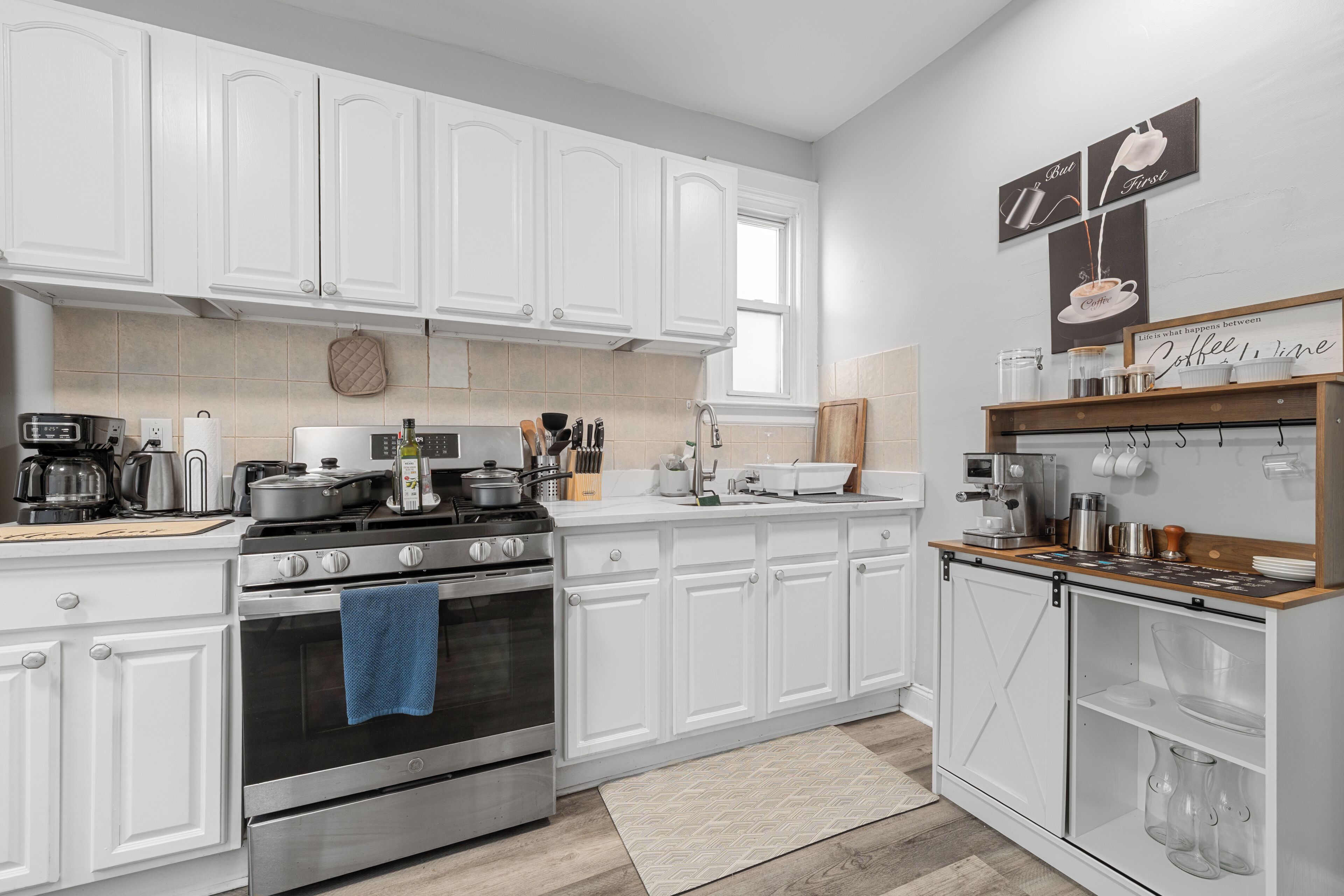 A modern kitchen with white cabinetry, a built-in oven, a coffee station, and a coffee machine.