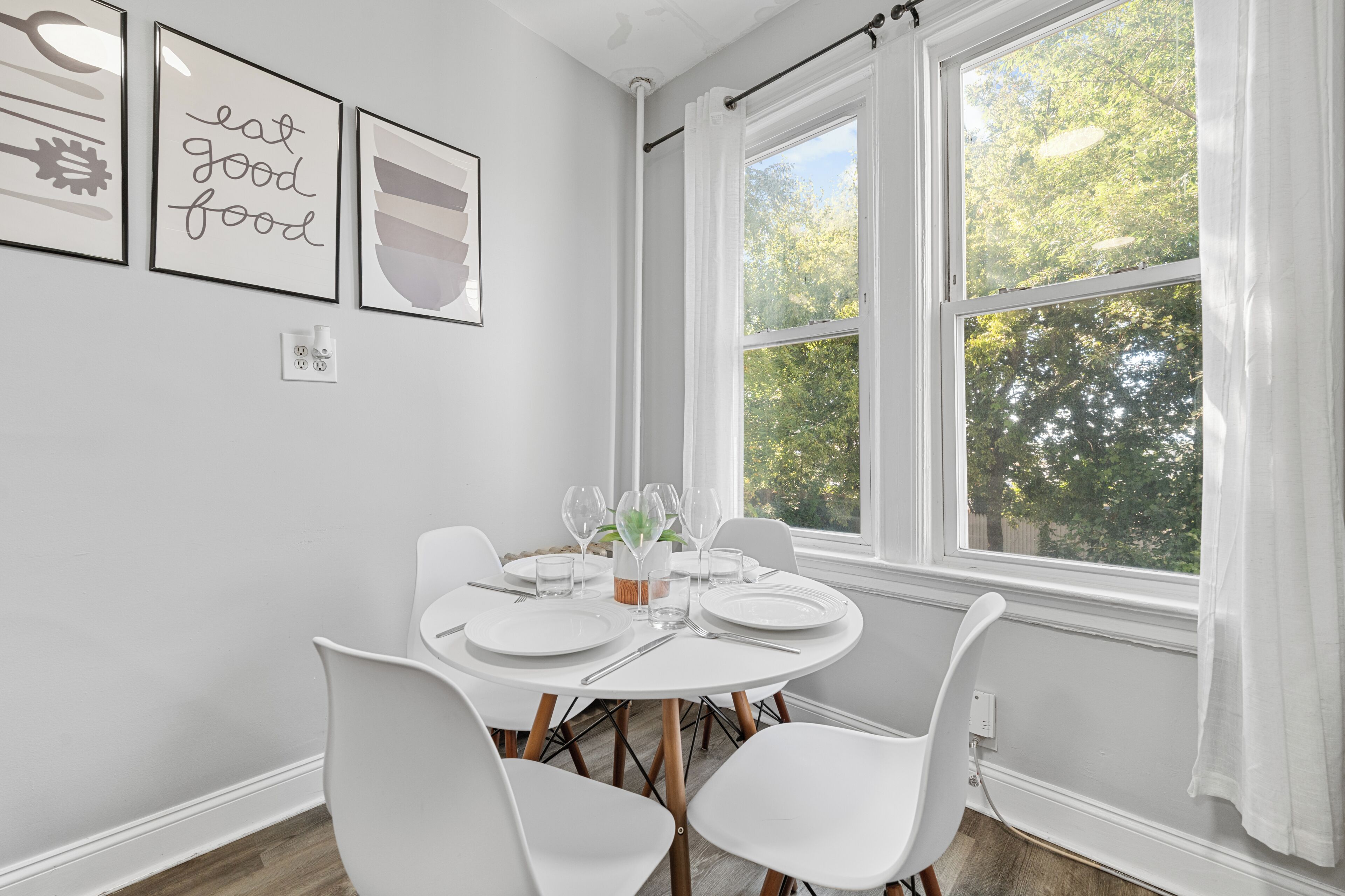 A dining area with a round table set for four, white chairs, and a window with curtains.
