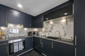 A modern kitchen with dark cabinetry, a marble backsplash, and stainless steel appliances. - Chapel Street Suite - Grampian Lettings (Aberdeen)