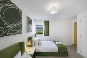 Ein Schlafzimmer mit einem Bett, einem Nachttisch, einer Lampe und Kunstwerken an den Wänden.
