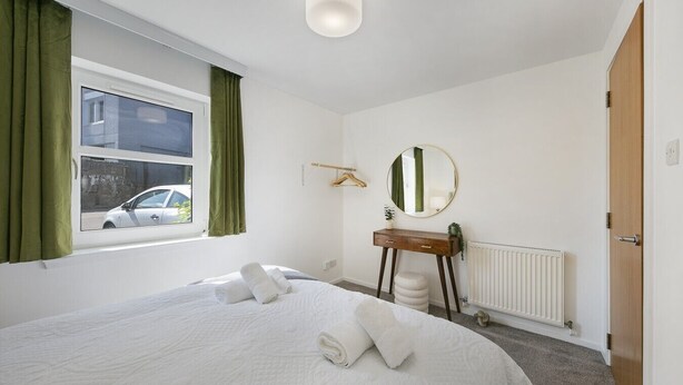 Ein Hotelzimmer mit einem Bett, einem Nachttisch, einem Spiegel, einem Heizkörper und einem Fenster mit Vorhängen.