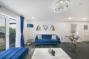 A modern living room with a blue sofa, a coffee table, and a chandelier. - Chapel Street Suite - Grampian Lettings (Aberdeen)