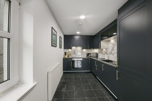 A narrow kitchen with dark cabinets, a white countertop, and a tiled floor. - Chapel Street Suite - Grampian Lettings (Aberdeen)