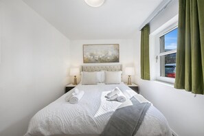 Ein Hotelzimmer mit einem Bett, zwei Nachttischen mit Lampen, einem Bild an der Wand und einem Fenster mit Vorhängen.