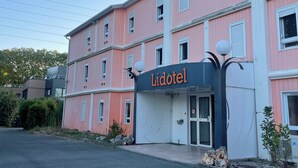 Un bâtiment rose avec une enseigne indiquant « Lidotel » et une entrée fermée par un portail.