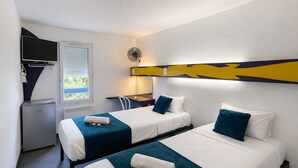 Une chambre d’hôtel avec deux lits, un bureau, une chaise, un petit réfrigérateur et une fenêtre avec des stores.
