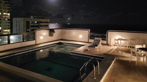 Un área de piscina en la azotea con vista al océano y una luna llena en el cielo.