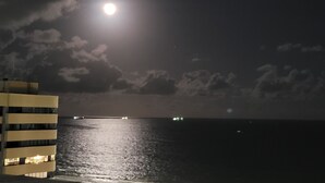 Escena nocturna con luna llena, un cuerpo de agua y un edificio con ventanas iluminadas.