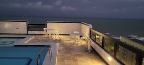 Ein Poolbereich auf dem Dach mit Blick auf das Meer, inklusive Pool, Liegestühlen und einem kleinen Tisch.