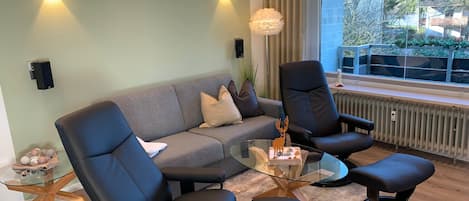 A modern living room with a sofa, two armchairs, a glass coffee table, and a view of the outdoors.