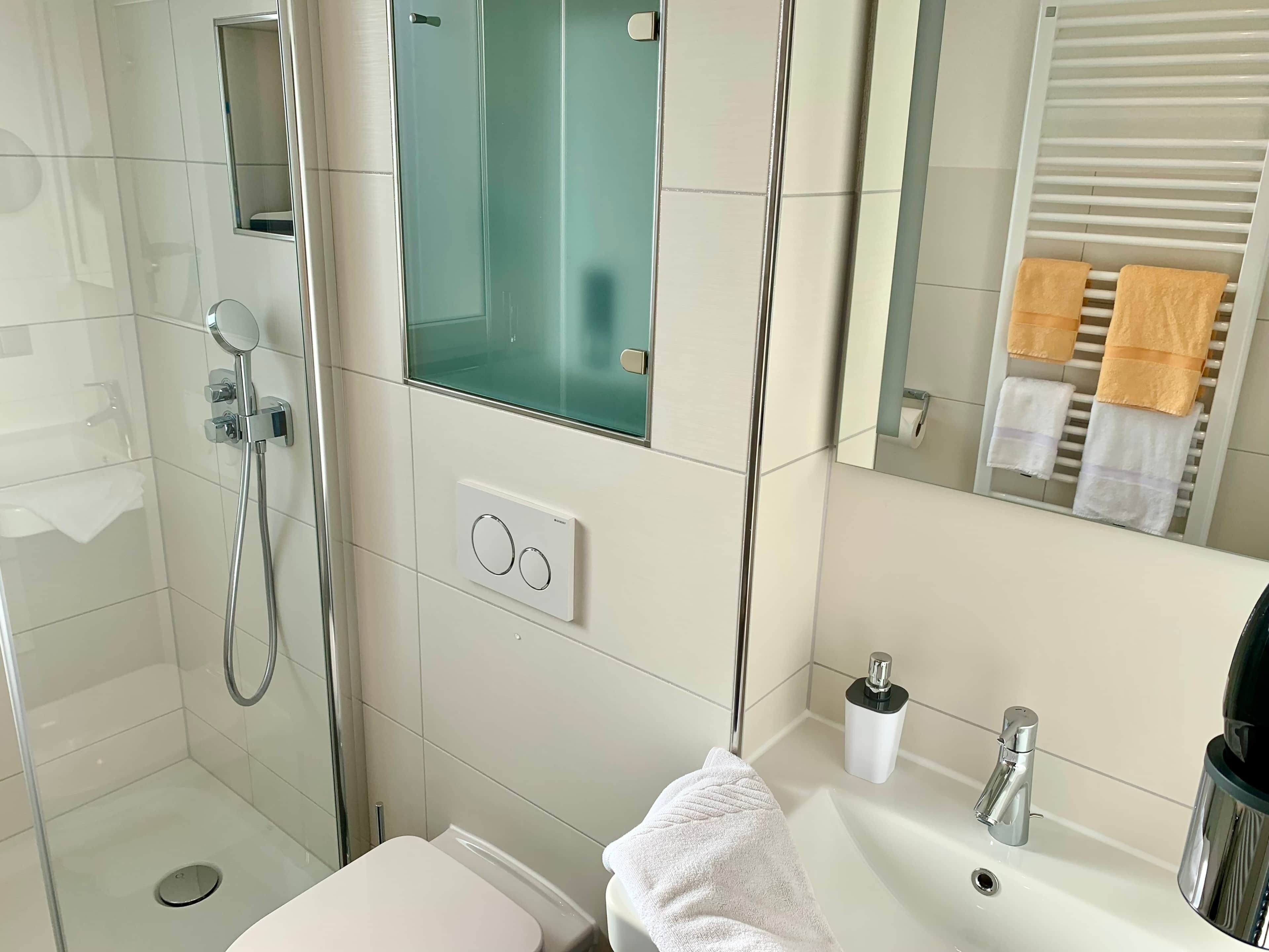 A modern bathroom with a glass-enclosed shower, a white sink with a mirror above it, and a towel rack with multiple towels.
