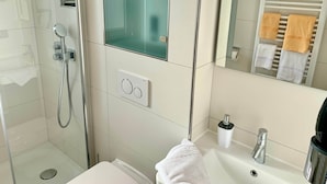 Un bagno moderno con doccia vetrata, un lavandino bianco con specchio sopra e un portasciugamani con diversi asciugamani.