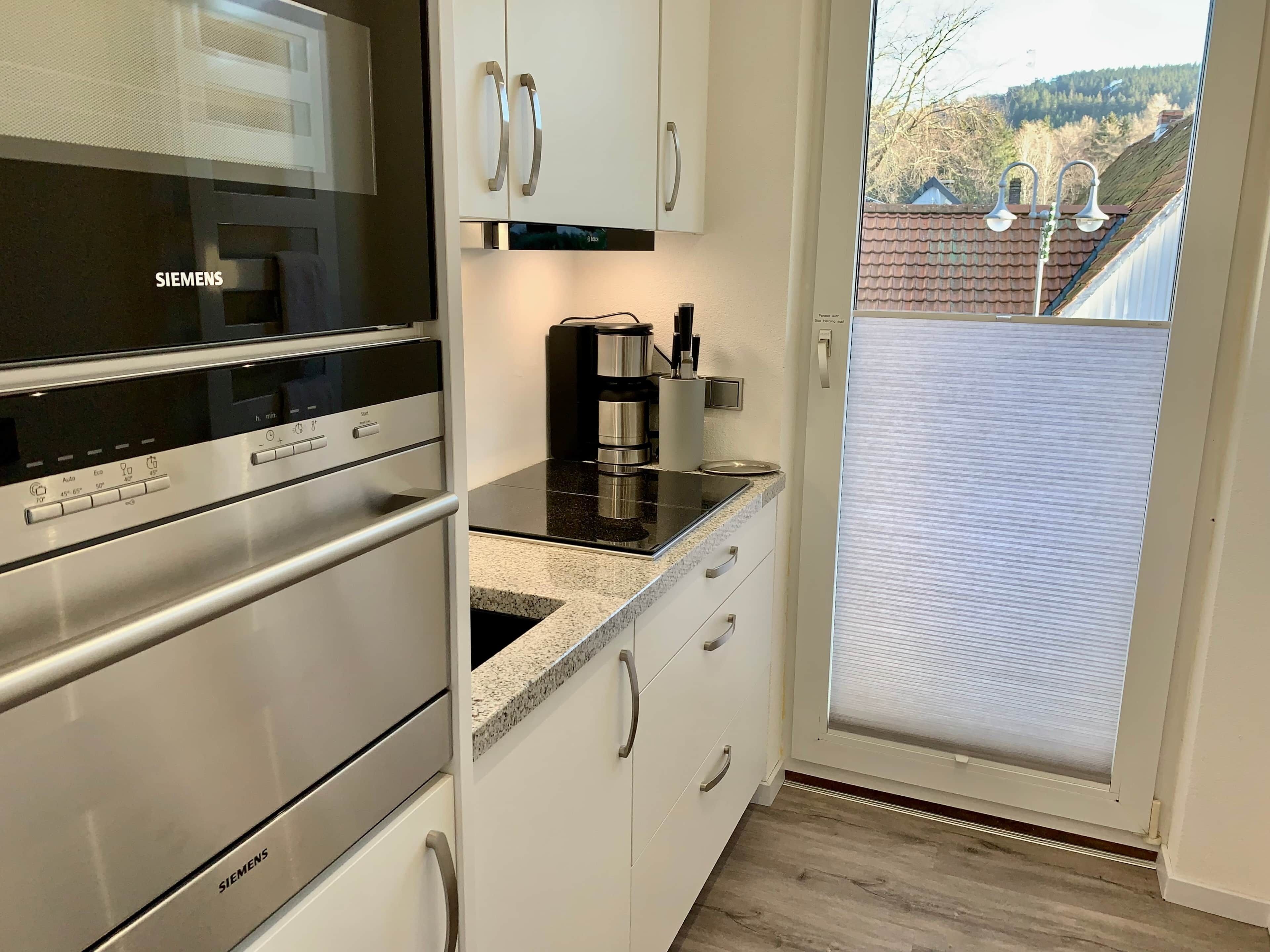 A kitchen with a Siemens oven, a coffee maker, and a view of a residential area through a glass door.