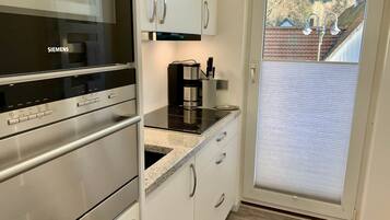 A kitchen with a Siemens oven, a coffee maker, and a view of a residential area through a glass door.
