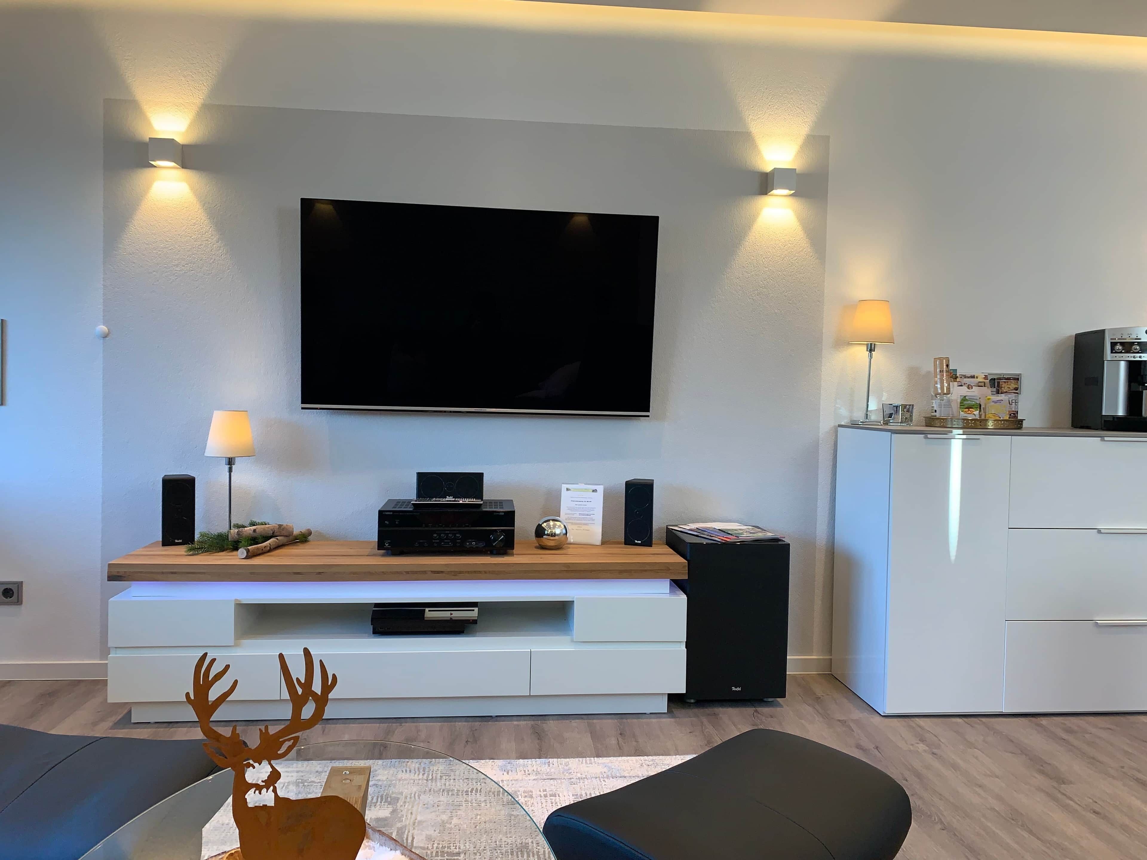 A modern living room with a flat-screen TV, a wooden entertainment unit, a white cabinet, and a glass coffee table.