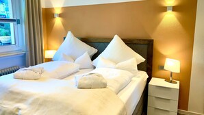 Una camera d'albergo con un letto, cuscini, un comodino e due lampade a parete.