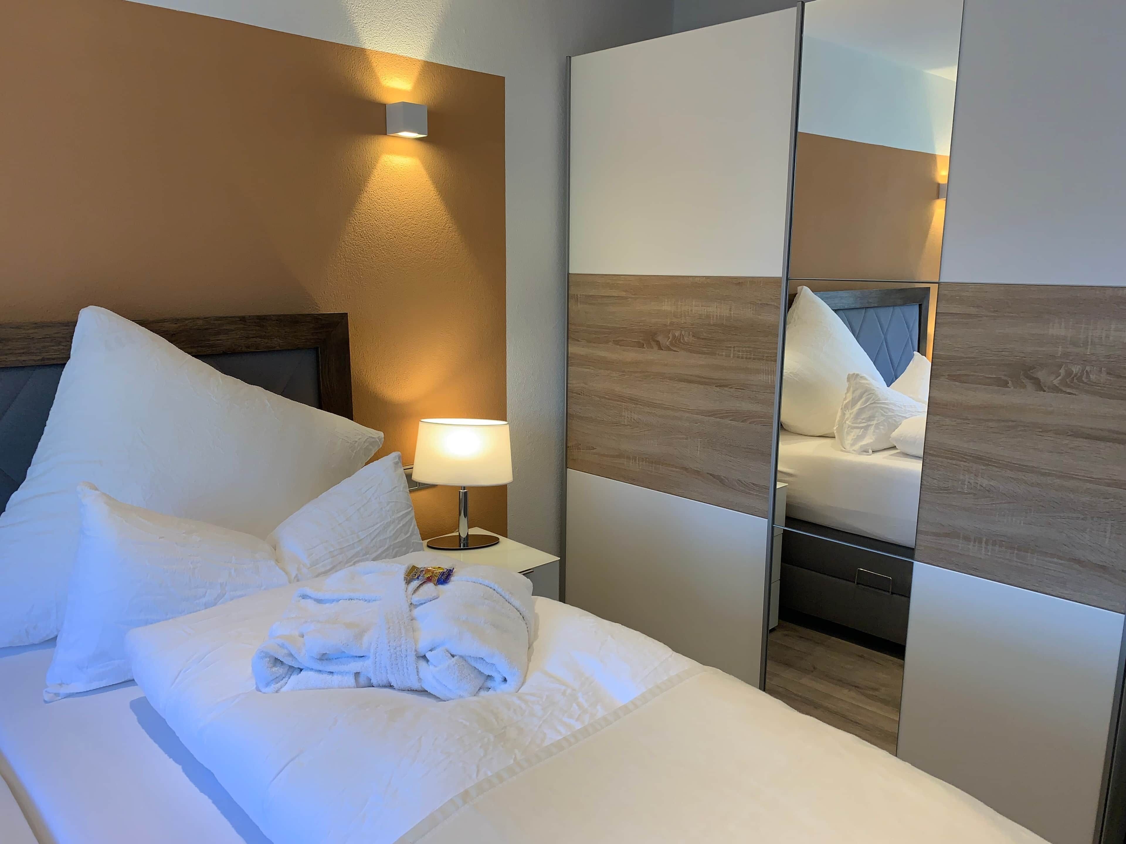 Hotellihuone, jossa on sänky, yöpöytälamppu, peili ja puinen pääty.
